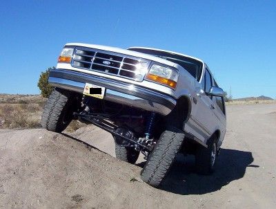 1995 Ford Bronco - This 1995 Ford Bronco is shown with its front wheels on a dirt mound, highlighting its lifted suspension and off-road capabilities.