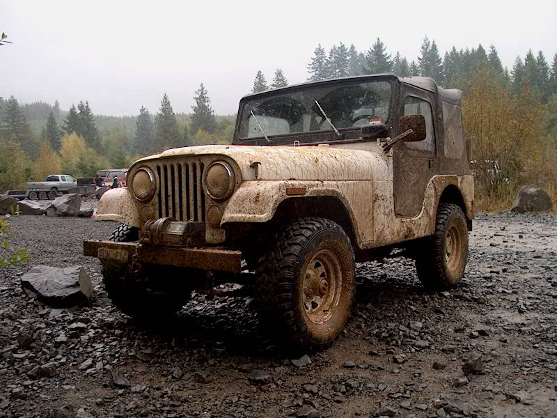 Muddy white Jeep CJ5 with black soft top, winch, and mud tires on wet rocky terrain