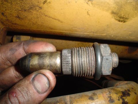 1966 International School Bus - A close-up view of a brass engine sensor being held by a dirty hand.