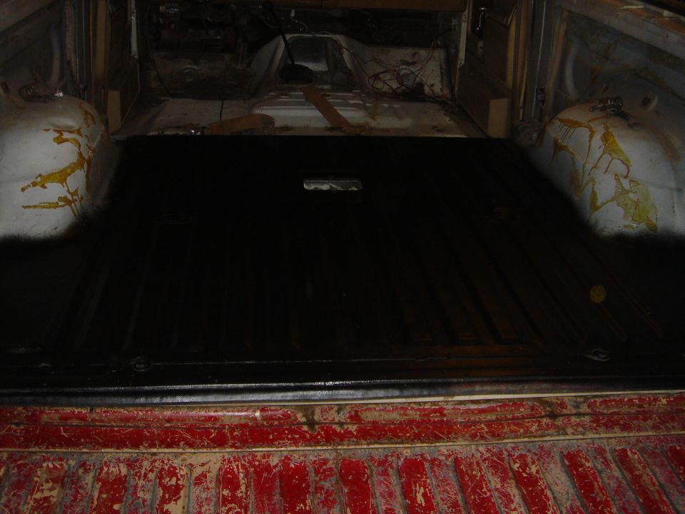 Stripped Bronco interior cargo floor painted black, bare front floor pan and worn red tailgate visible