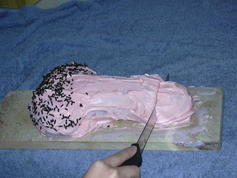 1997 Ford Probe - A pink-frosted cake with chocolate sprinkles sits on a wooden board over a blue towel, with a hand holding a knife to cut it. This is food,…