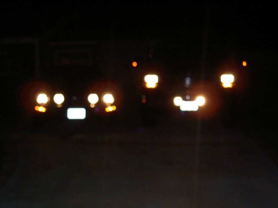 Two cars at night, one with four headlights and a license plate, the other with two headlights