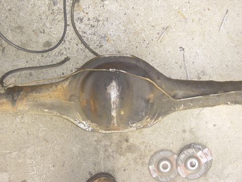 1989 Ford Bronco - A rear axle differential assembly with brake lines is shown, resting on a concrete surface with cutting discs nearby.