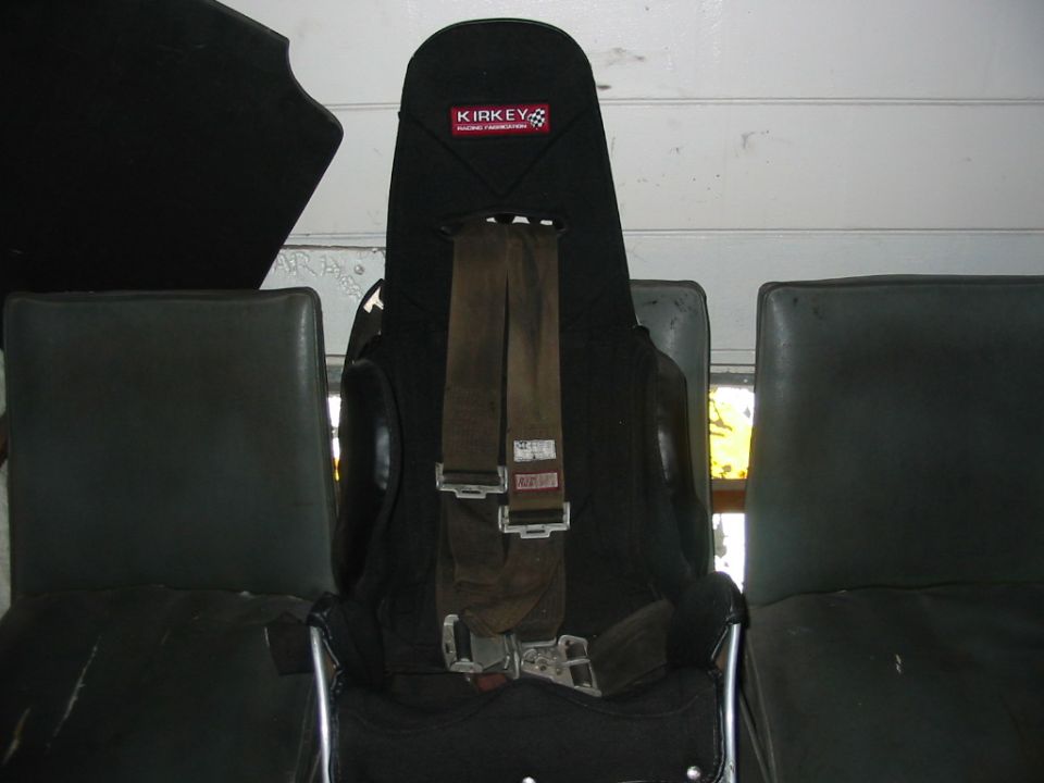 Black Kirkey aluminum racing seat with brown 5-point harness between two stock bucket seats