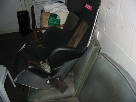 1985 Ford Crown Victoria LTD - A racing seat is placed over a car seat, with various items in the background.