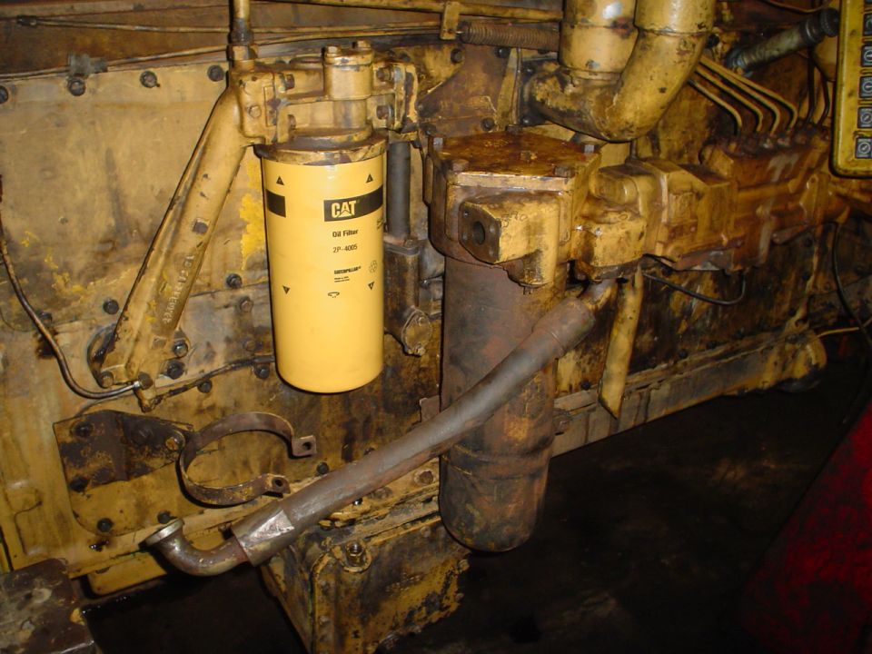 Yellow CAT oil filter and rusty metal pipe on a dirty engine block