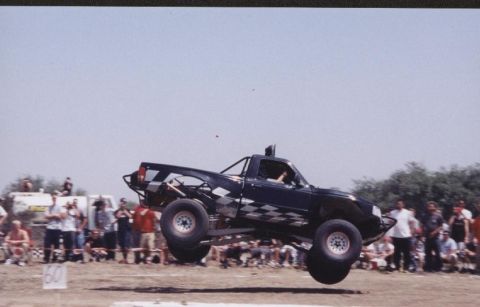 1984 Ford Bronco - A modified pickup truck soars through the air, performing a stunt for spectators.