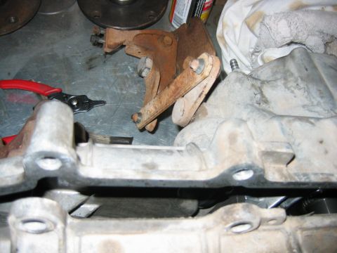 1992 Ford Bronco - Automotive parts laid out on a concrete garage floor, including a rusty cast bracket or mount, aluminum housings, a red-handled snap-ring p…