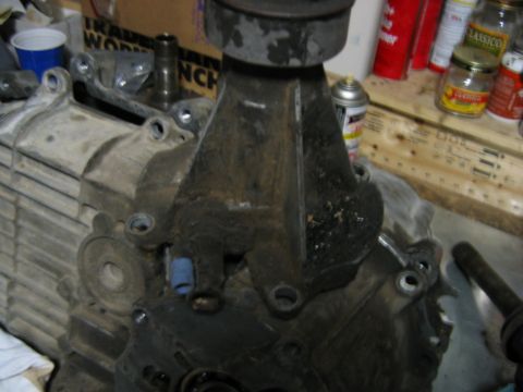 1992 Ford Bronco - A dirty cast-aluminum and steel manual transmission/transfer case assembly sitting on a workbench, viewed from the bell-housing side with b…