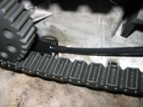 1992 Ford Bronco - Close-up of a gray toothed drive gear meshing with a segmented gray track or belt, with black cables routed nearby, set on a dusty concrete…