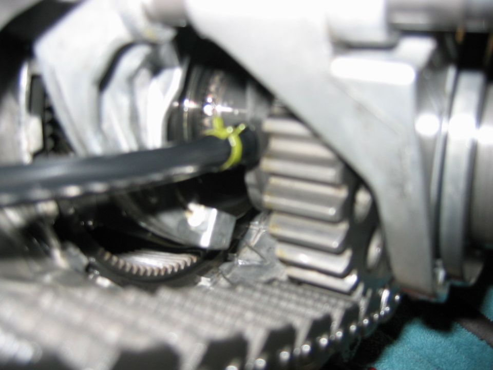 Close-up of an engine timing chain area showing gears, a cam sprocket, and a yellow timing mark