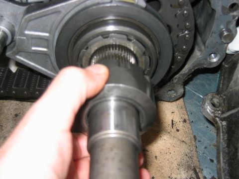 1992 Ford Bronco - Close-up of a hand holding a splined output shaft or yoke stub extending from a transmission or transfer case housing, with a chain and gea…