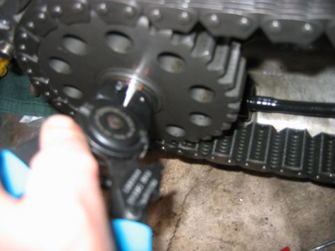1992 Ford Bronco - Close-up of a hand using a blue-handled ratchet on a large timing or gear sprocket, with a metal chain wrapped around it and a black hose v…