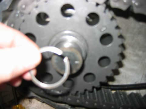 1992 Ford Bronco - Close-up of a metal timing gear or sprocket mounted on a splined shaft with a central bolt and washer, while a hand holds a metal snap ring…