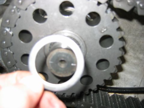 1992 Ford Bronco - Close-up of a timing gear/camshaft sprocket with a timing chain wrapped around it, viewed through a metal alignment tool or bushing held by…