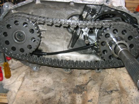 1992 Ford Bronco - Interior of a transfer case showing two large sprockets connected by a heavy-duty drive chain, with the output shaft protruding at right. T…