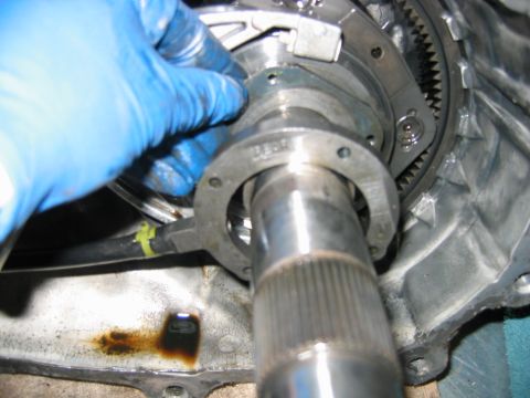 1992 Ford Bronco - Blue-gloved hand working on the splined output shaft and bearing retainer of a disassembled transmission, with the aluminum case, ring-gear…
