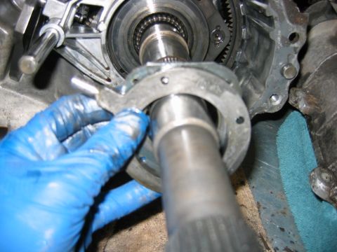 1992 Ford Bronco - Drivetrain rebuild in progress: a blue-gloved hand fits a stamped-steel bearing retainer plate over the output shaft of an opened transmiss…