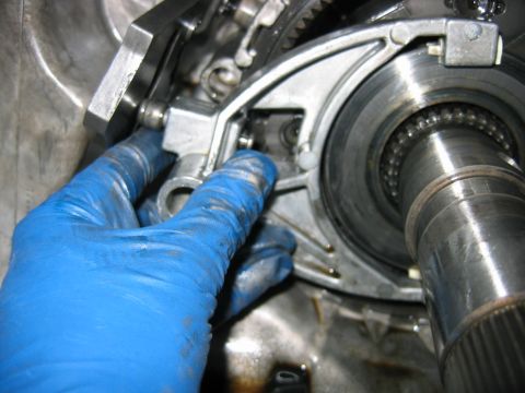 1992 Ford Bronco - A blue-gloved hand reaches into an opened transmission during a rebuild, beside a splined output shaft with an exposed roller bearing and a…