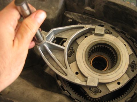 1992 Ford Bronco - Close-up of an automatic transmission's front pump/stator assembly being removed or installed, with a hand guiding a metal shaft into the s…
