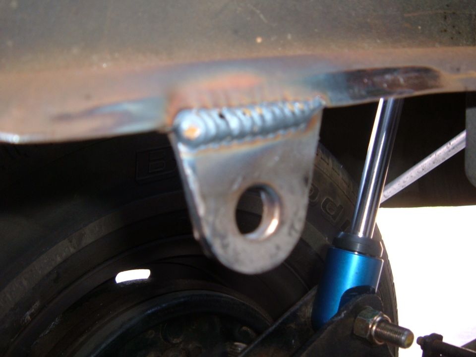 Welded bracket on vehicle frame near tire and blue shock absorber