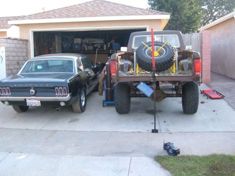 1985 Ford Ranger - A black 1967 Ford Mustang is parked next to a brown pickup truck in front of a garage.