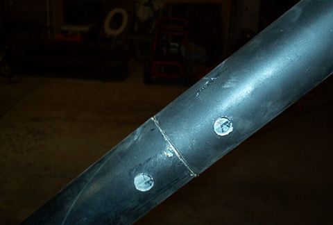 1986 Ford Bronco - Detail of black roll cage tubing, showing a welded joint and two circular decals with faint markings.