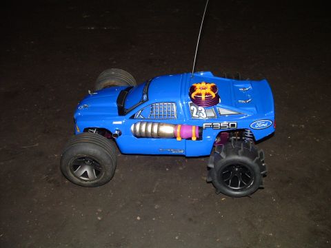 1994 Ford Bronco - A blue remote control monster truck with oversized tires and decorative exhaust pipes is shown from a 3/4 front angle.