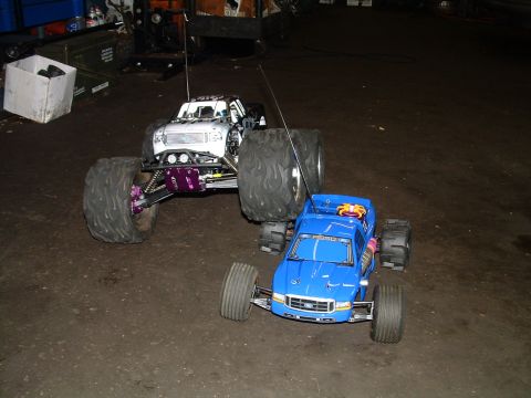 1994 Ford Bronco - Two remote control monster trucks, one a blue Ford F-350, are parked indoors on a concrete floor.