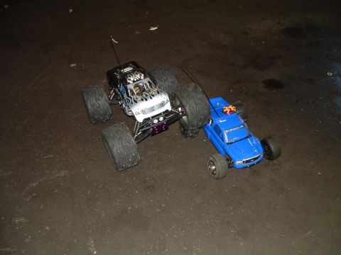 1994 Ford Bronco - Two remote control monster trucks are positioned on a dark surface.