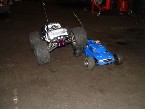 1994 Ford Bronco - Two RC trucks are parked on a garage floor, one is a large monster truck and the other is a smaller pickup truck.