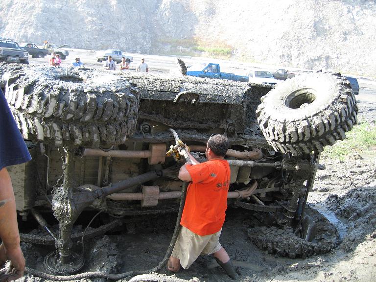Off-road vehicle overturned in mud with people around it. Other vehicles visible in background