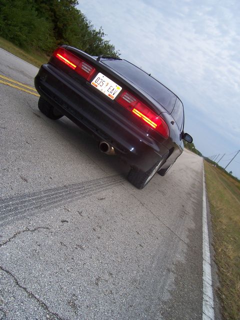 1994 Ford Probe - A black car with distinctive horizontal taillights drives down a road, leaving tire marks.