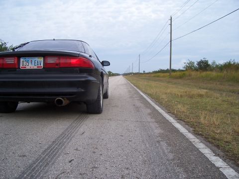 1994 Ford Probe - A black coupe is parked on the side of a long, straight road with power lines overhead.