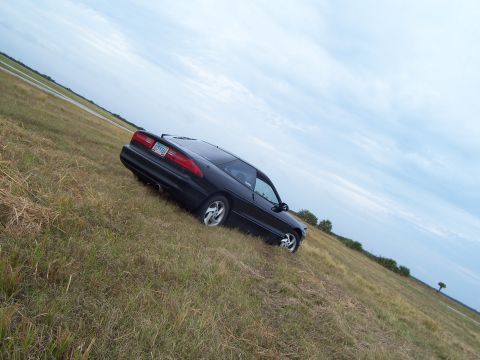 1994 Ford Probe - A black 1994 Ford Probe is parked on a grassy slope under a cloudy sky.
