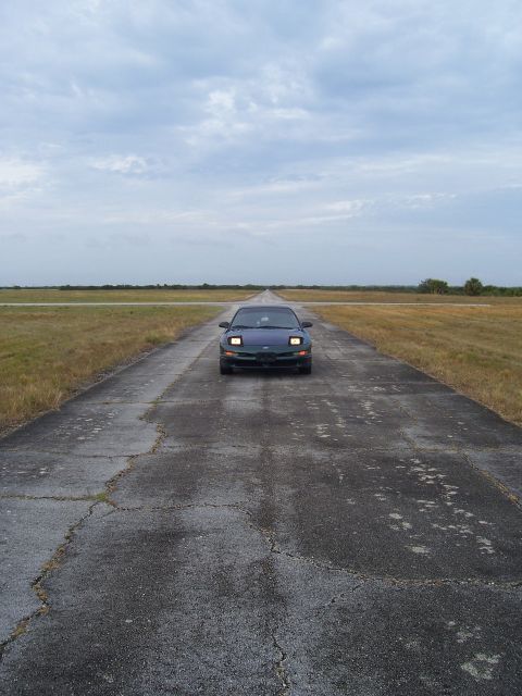1994 Ford Probe - A 1994 Ford Probe is parked on a desolate, cracked asphalt road under a cloudy sky.