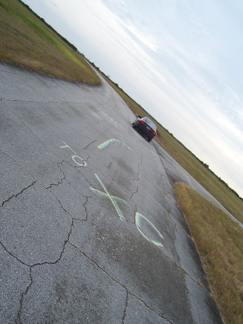 1994 Ford Probe - A dark sedan is parked on a cracked asphalt surface with chalk markings, under a cloudy sky.