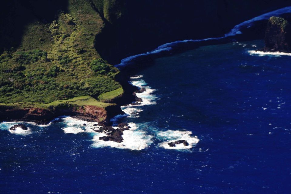 Ocean waves crash against rocky cliffs and a green, vegetated coastline