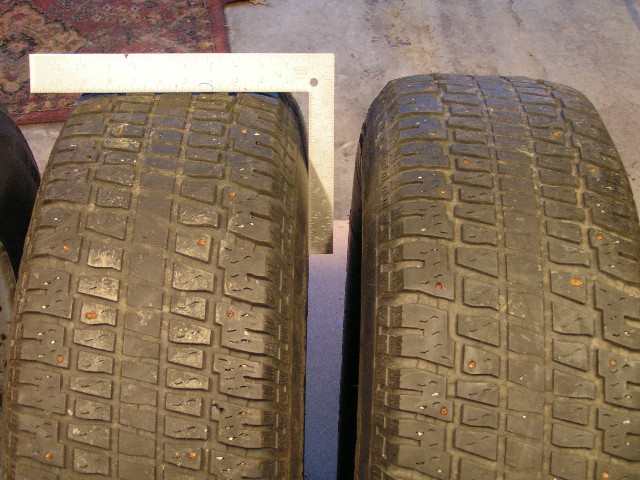 Close-up of two worn tire treads with a metal ruler laid across for scale