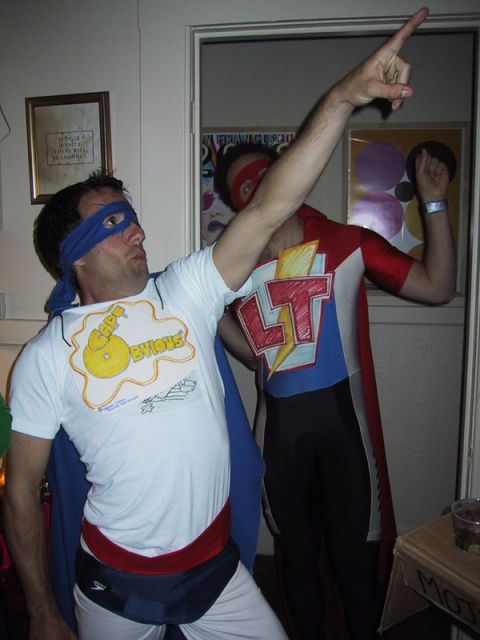 1991 Ford Bronco - Two individuals dressed as superheroes pose indoors, with one pointing upwards and the other displaying a lightning bolt emblem.