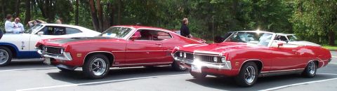 1970 Ford Torino - Three classic American muscle cars are parked side-by-side on a sunny day.