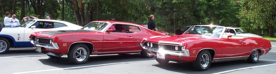 Red Ford Torino GT fastback and red Torino convertible parked beside a white fastback at a car show