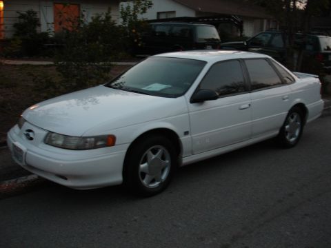 1995 Ford Taurus - A white 1995 Ford Taurus sedan is parked on the street in front of a house.