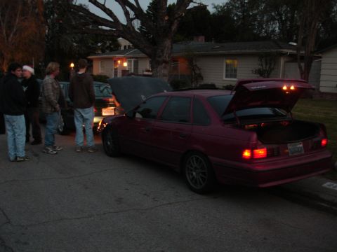 1995 Ford Taurus - A maroon 1995 Ford Taurus sedan is parked with its trunk and hood open, as a group of people stand nearby.