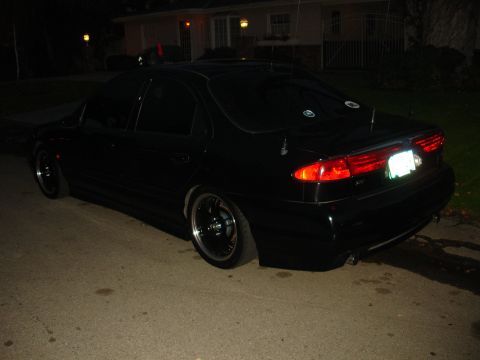 1995 Ford Taurus - Rear view of a black 1995 Ford Taurus sedan with aftermarket wheels parked on a street at night.