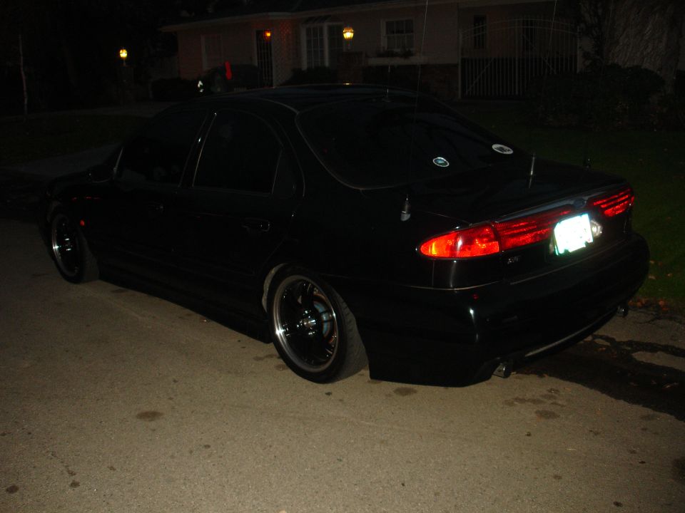 1995 Ford Taurus sedan, rear 3/4 view, black paint, aftermarket wheels, parked at night