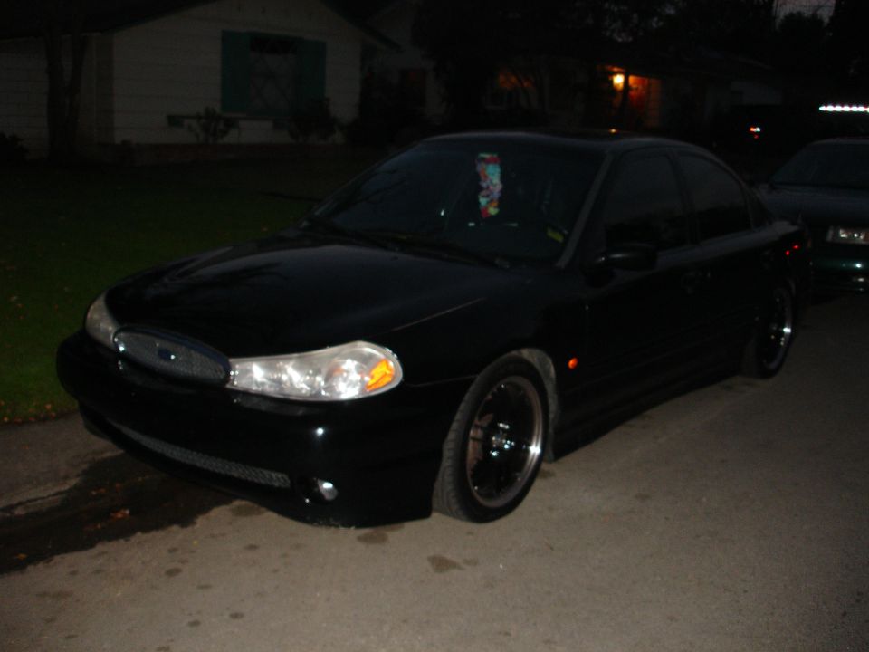 Black 1995 Ford Taurus sedan, front 3/4 view, parked on street at night