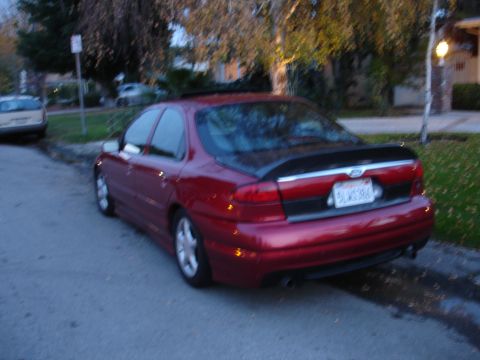 1995 Ford Taurus - Rear view of a red 1995 Ford Taurus sedan parked on a residential street, a black spoiler and a visible license plate.