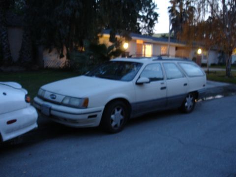1995 Ford Taurus - A 1995 Ford Taurus station wagon is parked on the street next to another vehicle.