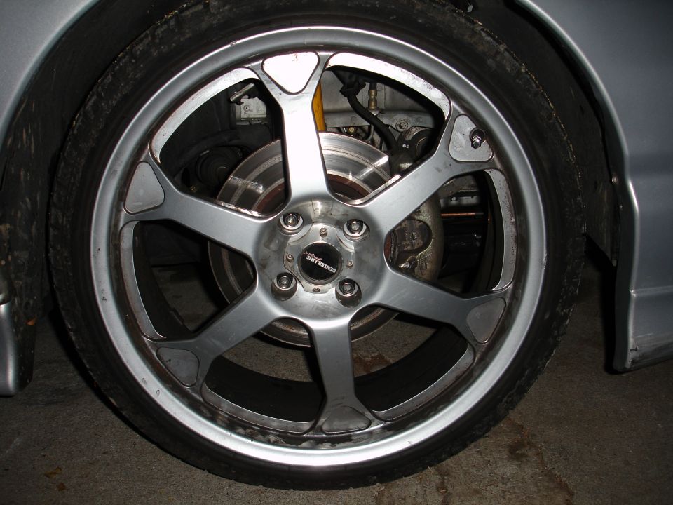 Silver five-spoke aftermarket wheel with a black center cap on a car tire
